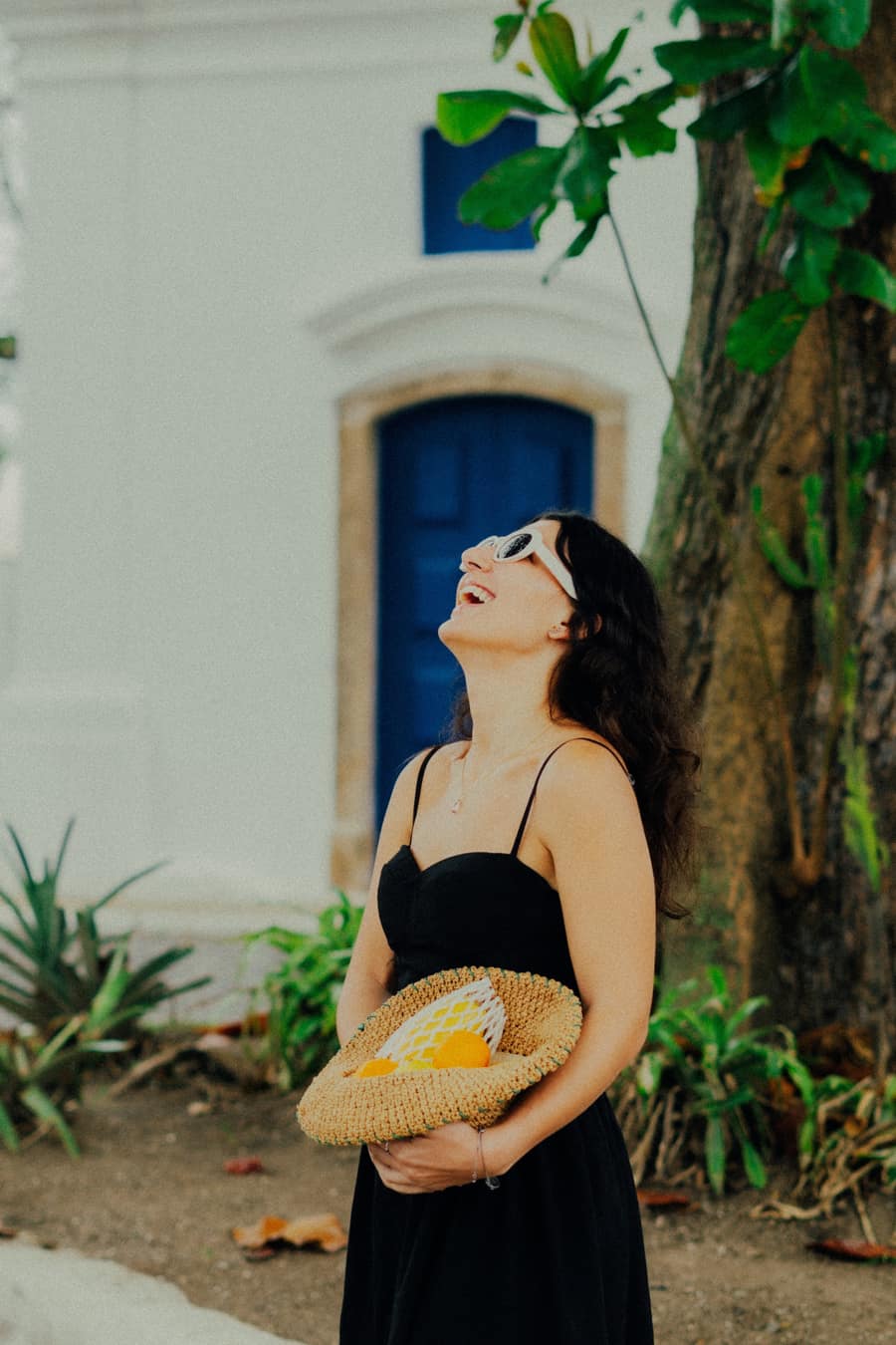 Amanda Butten rindo, com um chapéu de palha cheio de laranjas nas mãos